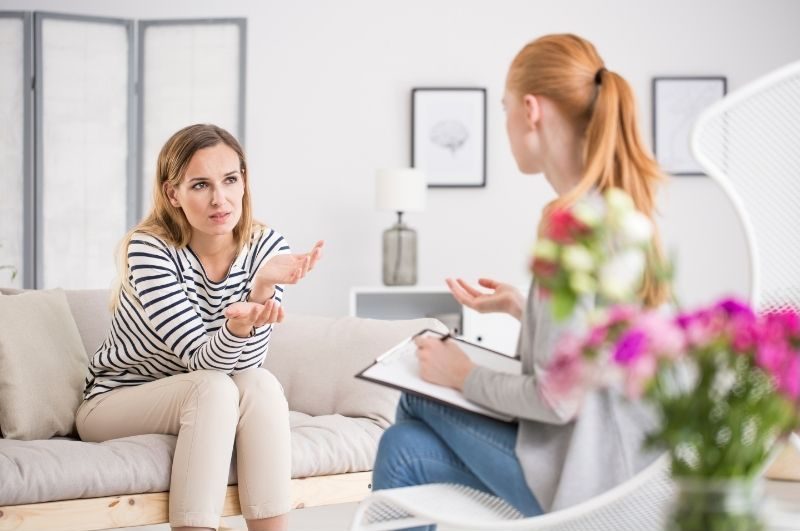 Dos mujeres jóvenes sentadas en el sofá hablando. Sesión psicoterapia